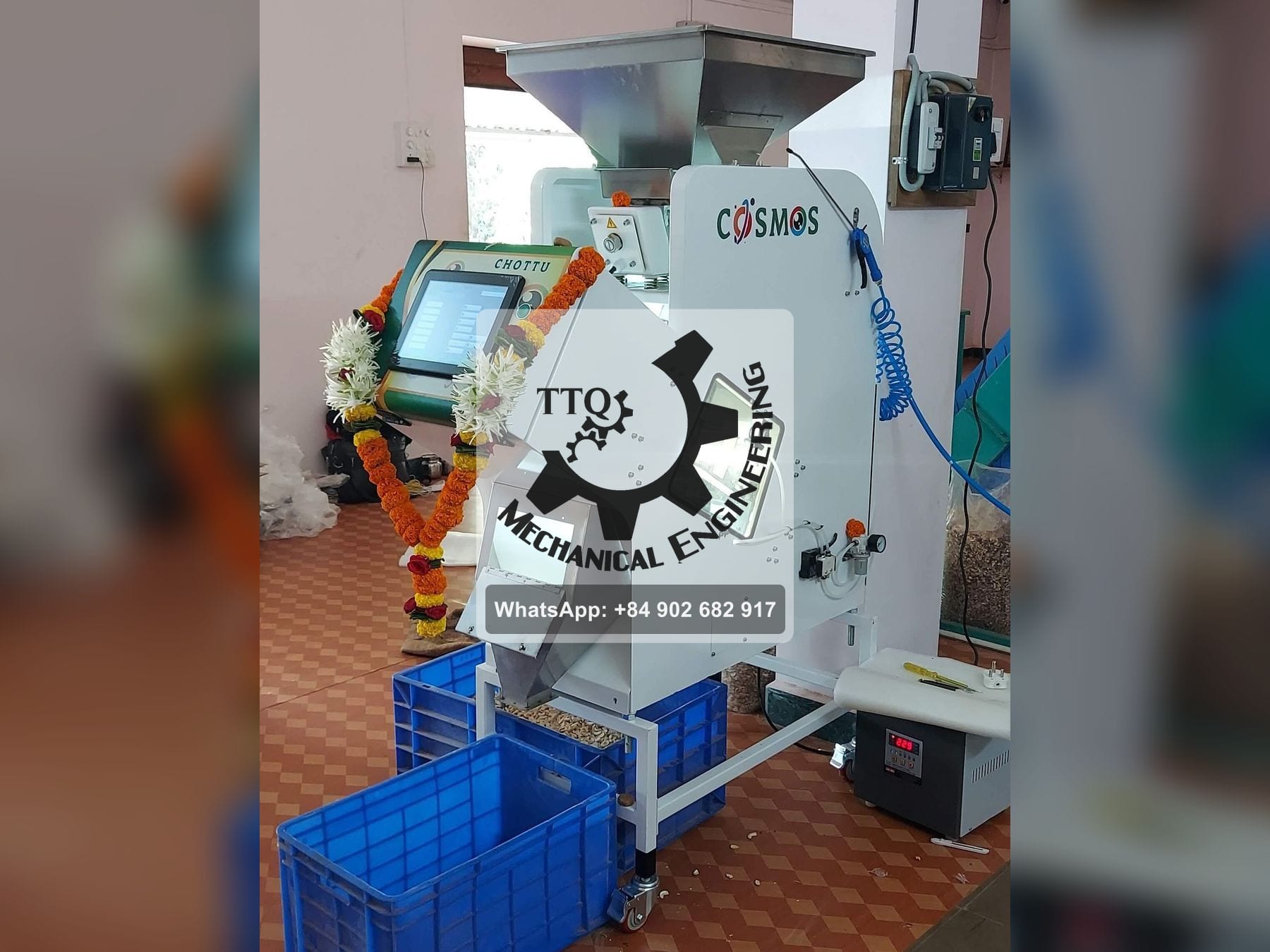 An optical colour sorter installed in a cashew plant, garlanded for its commissioning, with feed hopper, viewing window and touchscreen