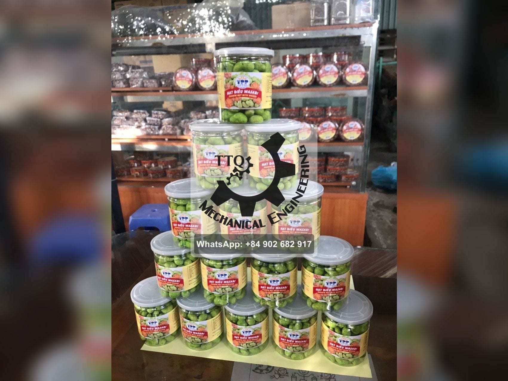 A pyramid of sealed retail jars of coated cashew kernels stacked on a shop counter