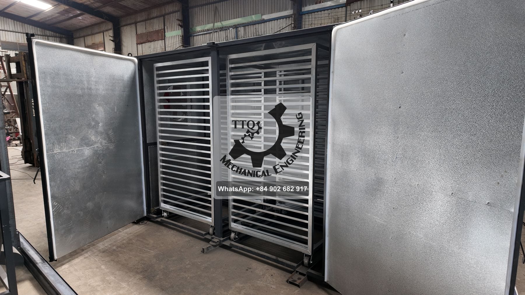 A tray dryer with doors open and two loaded trolleys inside